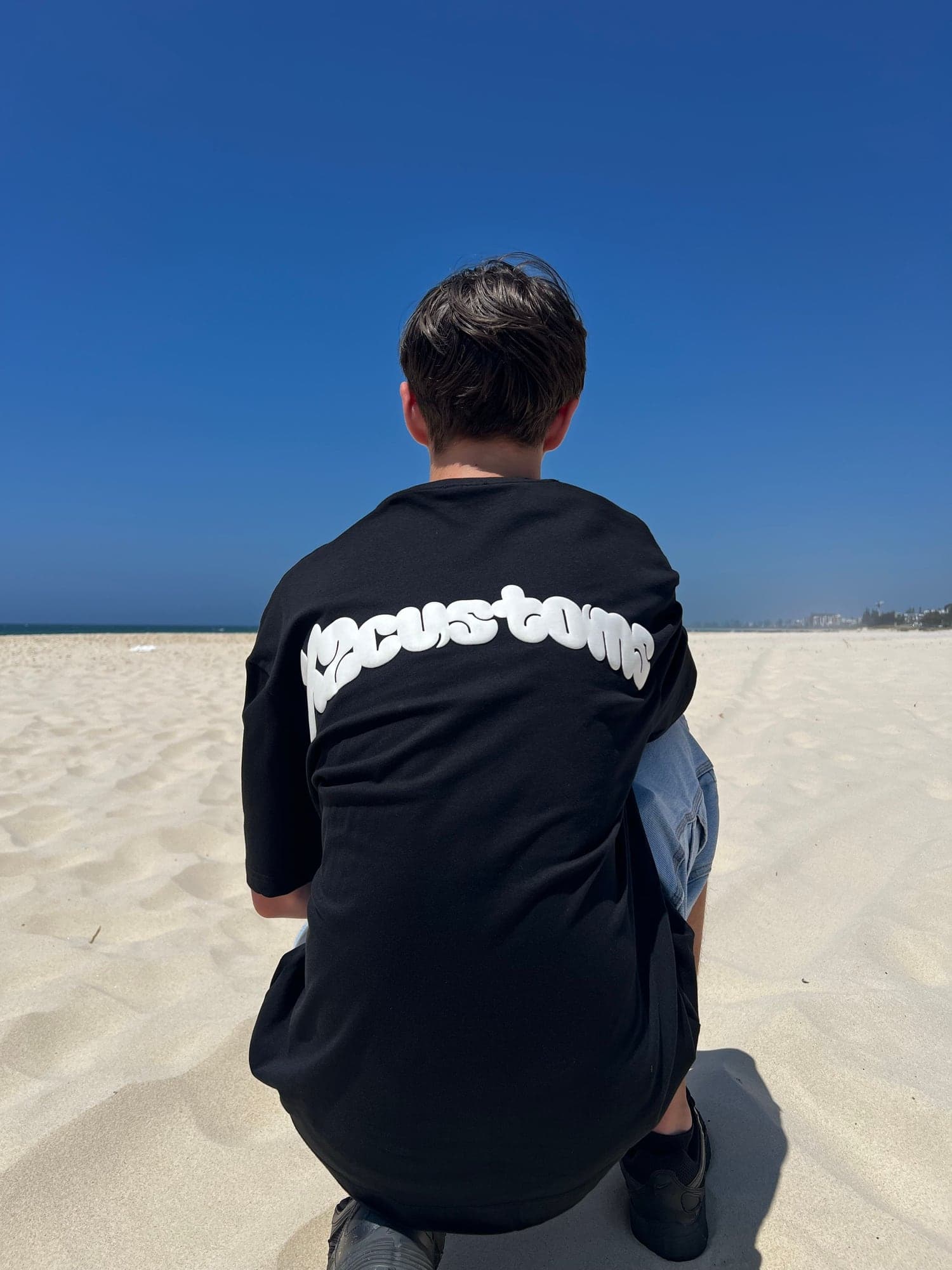 Rider crouched on the beach wearing the X2 Puff Print Tee, the X2customs back print showing